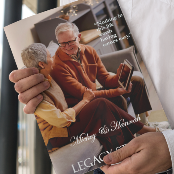 Person holding a custom legacy book titled ‘Mickey & Hannah’ featuring an elderly couple smiling warmly at each other with the quote ‘Nothing in this life worth having comes easy.