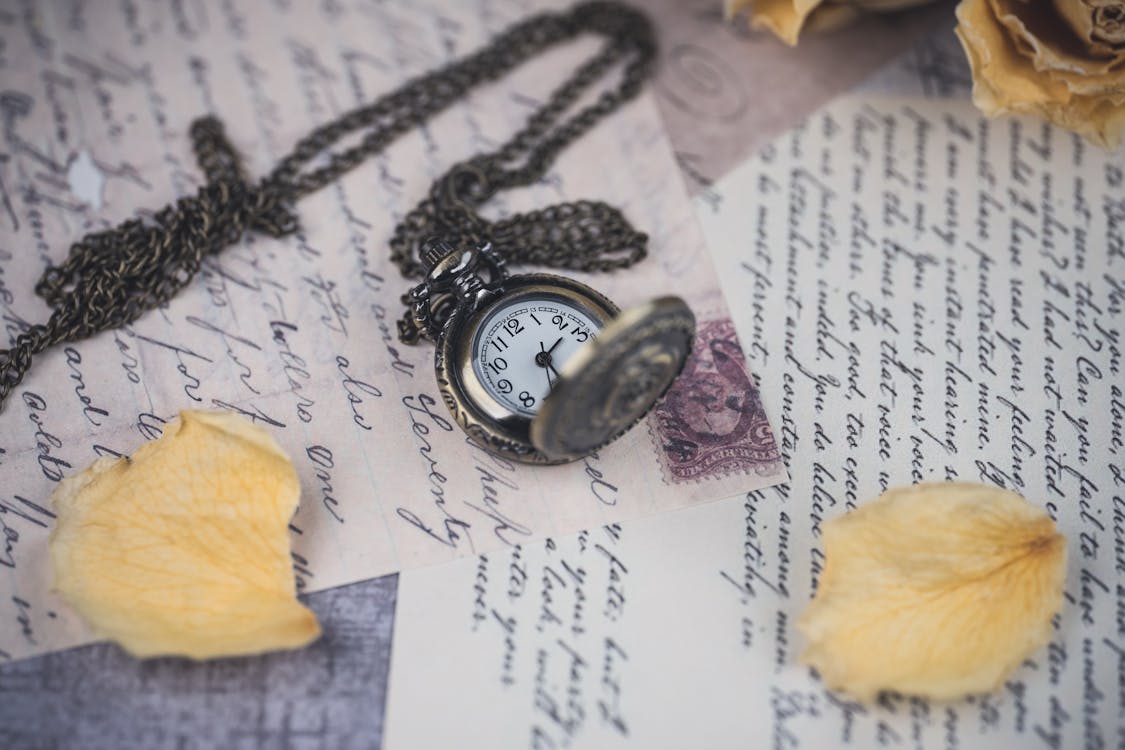 Vintage pocket watch resting on handwritten letters with dried yellow rose petals, symbolizing timeless memories and legacy.