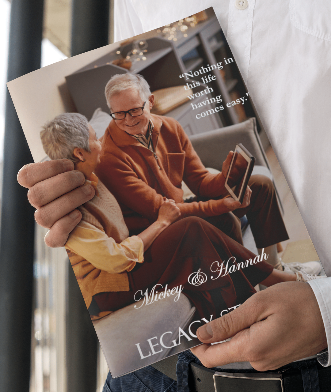 Person holding a custom legacy book titled ‘Mickey & Hannah’ featuring an elderly couple smiling warmly at each other with the quote ‘Nothing in this life worth having comes easy.